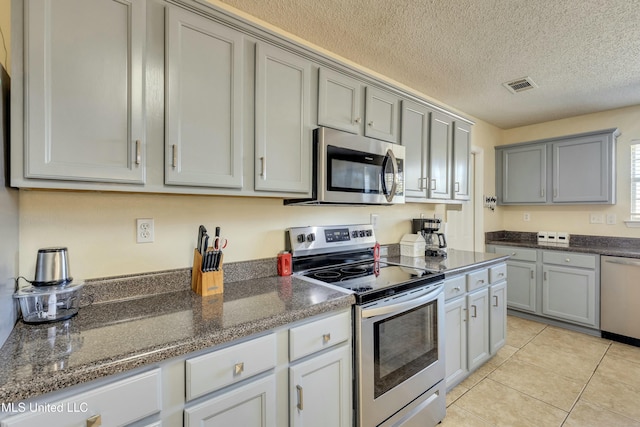 kitchen featuring a textured ceiling, gray cabinetry, light tile patterned floors, and stainless steel appliances