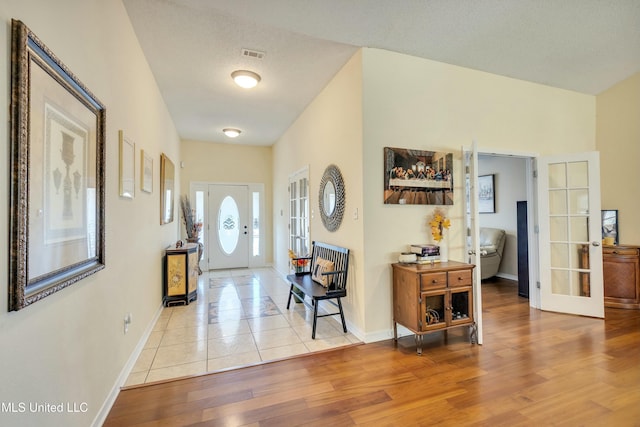 foyer with french doors, a textured ceiling, and light wood-type flooring