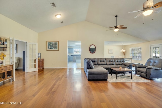 living room with ceiling fan with notable chandelier, vaulted ceiling, french doors, and light hardwood / wood-style flooring