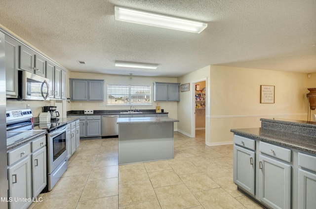 kitchen with sink, gray cabinets, light tile patterned floors, appliances with stainless steel finishes, and a kitchen island