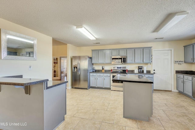 kitchen featuring gray cabinetry, light tile patterned floors, a textured ceiling, and appliances with stainless steel finishes