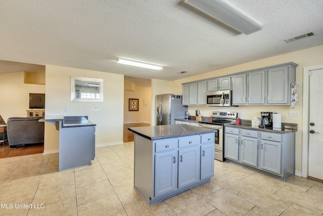 kitchen featuring a center island, light tile patterned floors, a textured ceiling, and appliances with stainless steel finishes