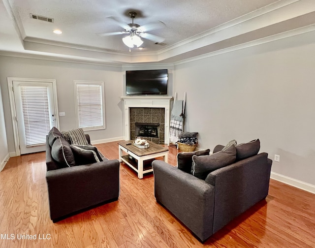 living room with a raised ceiling, ceiling fan, ornamental molding, and a textured ceiling