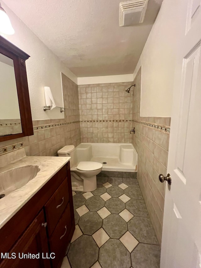 bathroom with tile walls, toilet, tiled shower, vanity, and tile patterned flooring