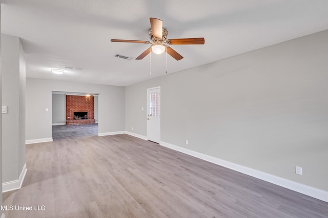 unfurnished living room featuring ceiling fan, a brick fireplace, and light wood-type flooring