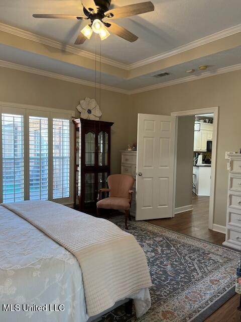 bedroom featuring a tray ceiling, dark wood-style flooring, crown molding, visible vents, and ceiling fan