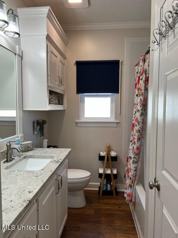 bathroom featuring baseboards, toilet, wood finished floors, crown molding, and vanity