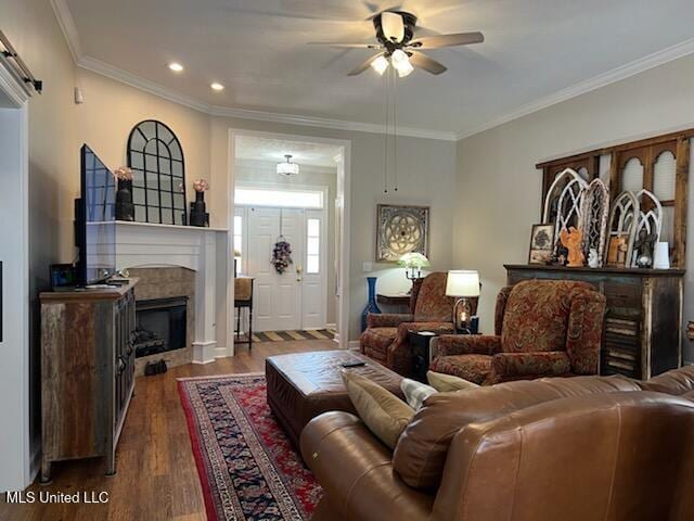 living room featuring a barn door, a ceiling fan, ornamental molding, dark wood-style flooring, and a fireplace