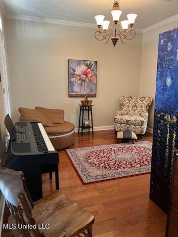 sitting room with crown molding, baseboards, wood finished floors, and an inviting chandelier