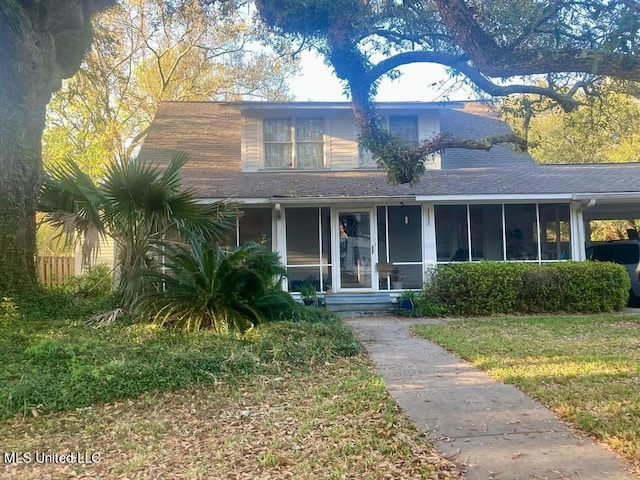 view of front of property featuring a front yard, a sunroom, and a shingled roof