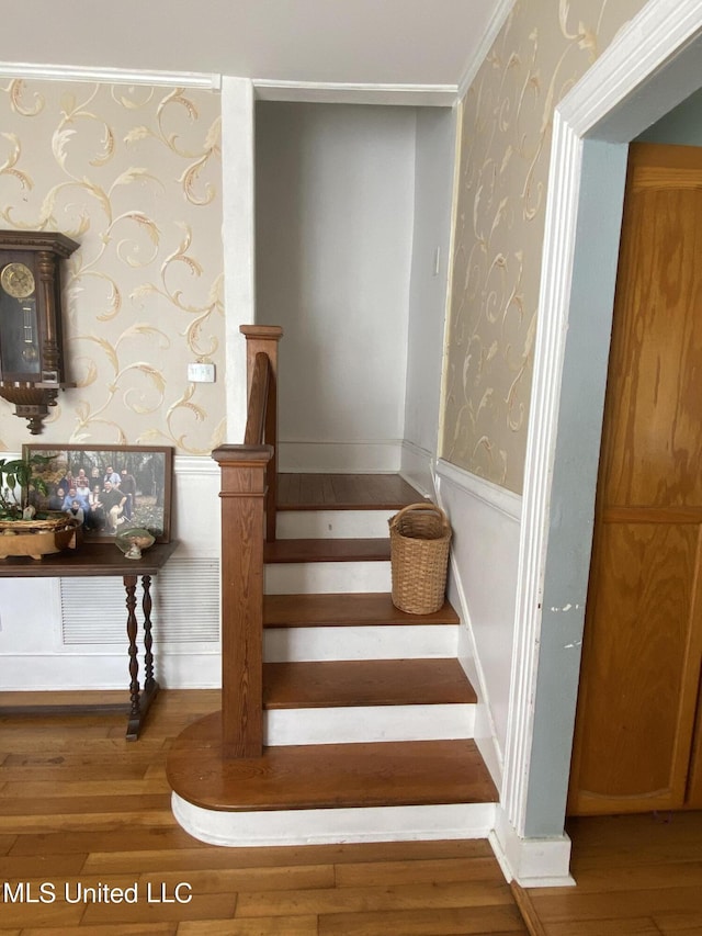 staircase with wood finished floors, wallpapered walls, and wainscoting