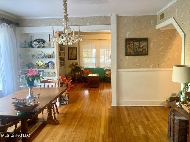 dining area featuring hardwood / wood-style flooring, a chandelier, visible vents, wallpapered walls, and wainscoting