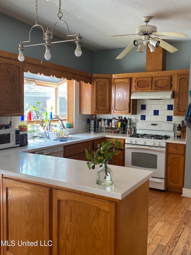 kitchen featuring white appliances, kitchen peninsula, sink, and light wood-type flooring