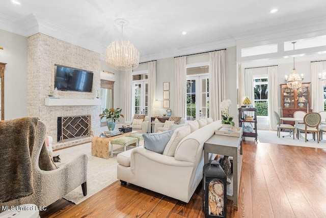 living room featuring a stone fireplace, crown molding, a notable chandelier, and wood-type flooring