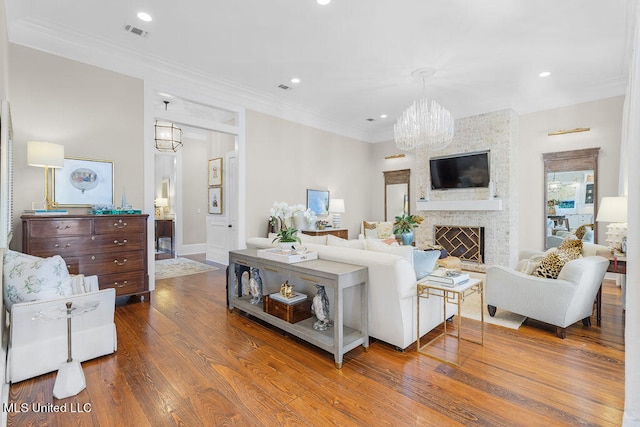 living room with a stone fireplace, crown molding, a chandelier, and wood-type flooring