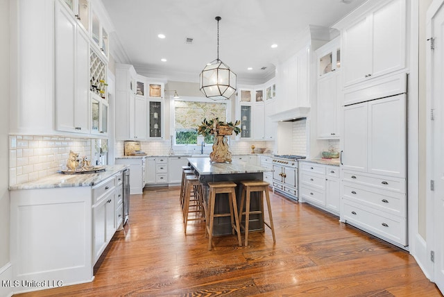 kitchen featuring crown molding, a kitchen island, white cabinets, dark wood-type flooring, and light stone counters