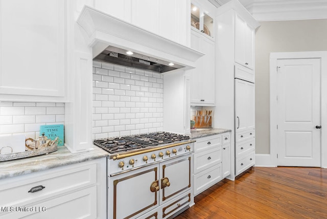 kitchen featuring tasteful backsplash, premium range hood, white cabinetry, wood-type flooring, and high end stainless steel range