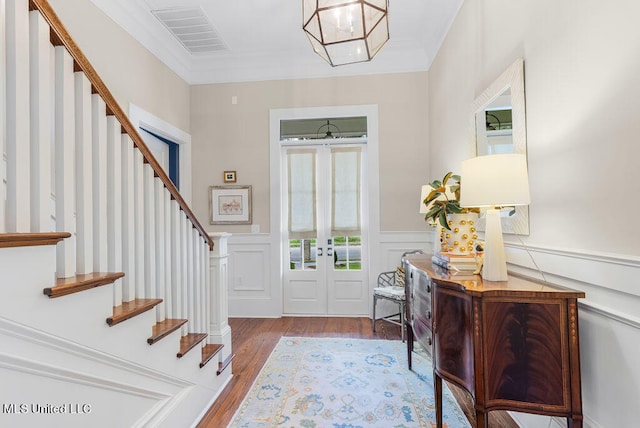 entrance foyer with french doors, a notable chandelier, crown molding, and light hardwood / wood-style floors