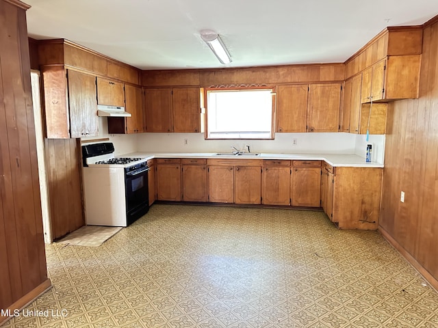 1628 Dry Creek Rd, Magee, MS 39111 - kitchen featuring range with gas stovetop, a sink, under cabinet range hood, brown cabinetry, and wood walls