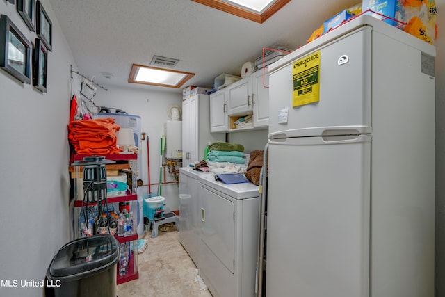 washroom with tankless water heater, washer and dryer, a textured ceiling, and cabinets