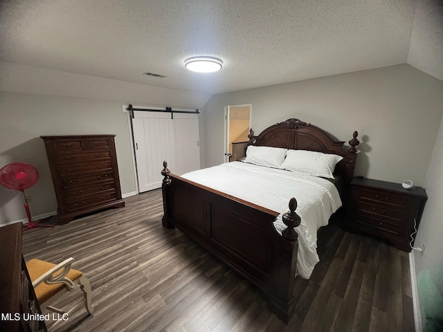 bedroom with a textured ceiling, a barn door, visible vents, lofted ceiling, and wood finished floors
