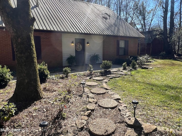 view of front of house featuring a patio area, brick siding, a front yard, and metal roof