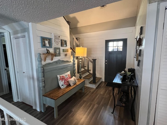 entryway with dark wood-style flooring, a textured ceiling, wooden walls, and stairs