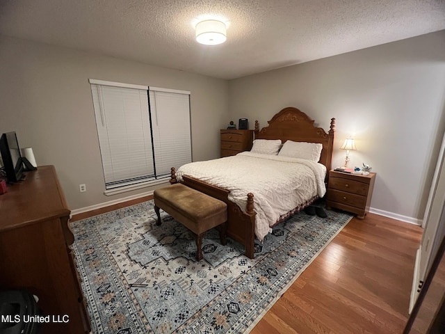 bedroom with baseboards, a textured ceiling, and wood finished floors