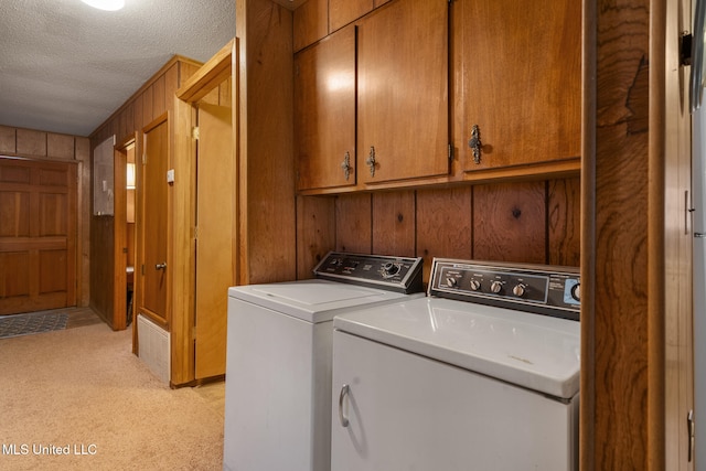 laundry area featuring cabinets, washing machine and dryer, a textured ceiling, and wooden walls