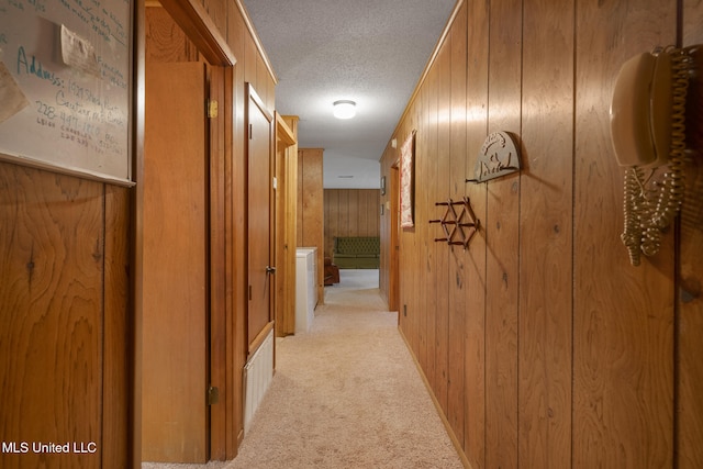 hallway with wooden walls, light carpet, and a textured ceiling