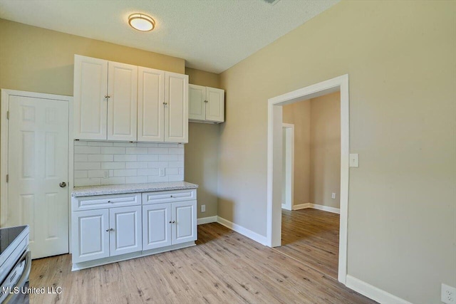 1204 Jackson St, Vicksburg, MS 39183 - kitchen with a textured ceiling, light wood-style flooring, backsplash, white cabinets, and baseboards