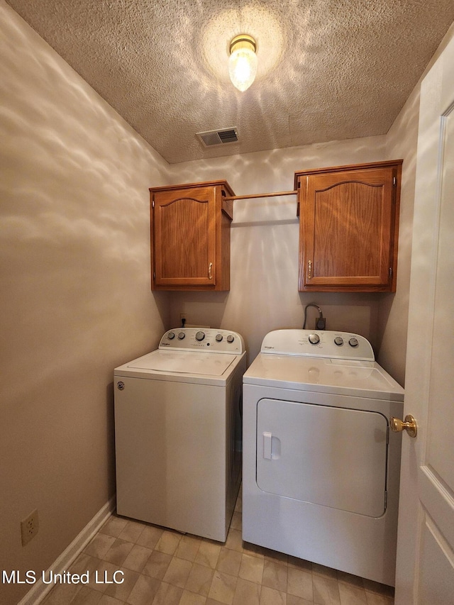 laundry area featuring washer and dryer, a textured ceiling, and cabinets