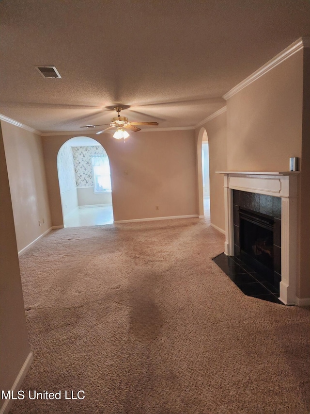 unfurnished living room with a tiled fireplace, dark carpet, ornamental molding, a textured ceiling, and ceiling fan