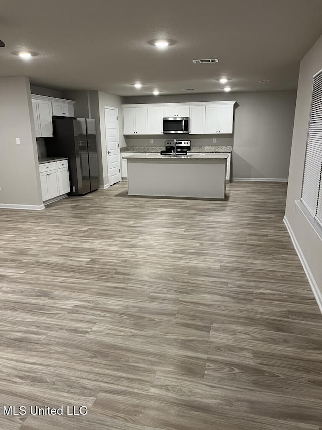 kitchen with stainless steel appliances, an island with sink, white cabinets, and light wood-type flooring