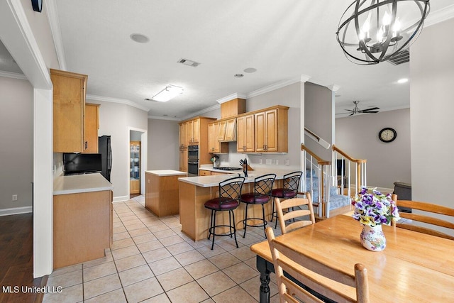 kitchen with hanging light fixtures, black double oven, light tile patterned flooring, ceiling fan with notable chandelier, and crown molding