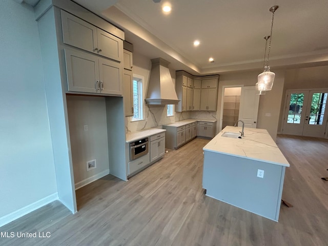 kitchen featuring wall chimney exhaust hood, decorative light fixtures, a wealth of natural light, and an island with sink