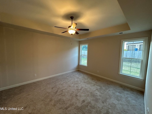 carpeted empty room with ceiling fan and a tray ceiling