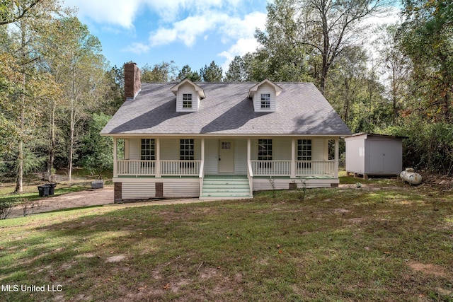 new england style home featuring covered porch, a front yard, and a storage shed