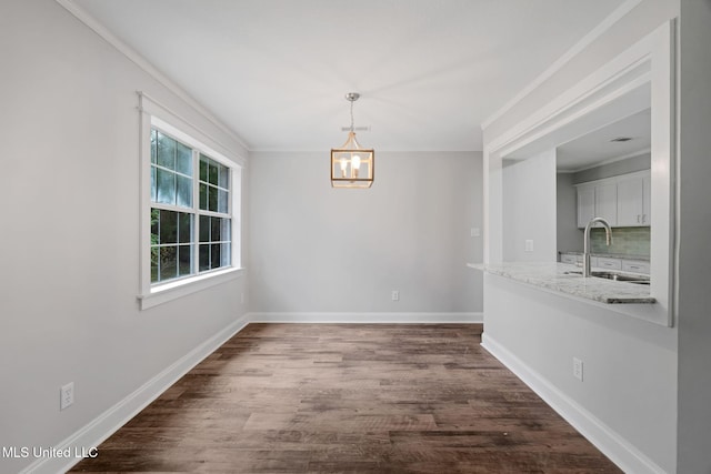 unfurnished dining area featuring dark hardwood / wood-style flooring, ornamental molding, sink, and an inviting chandelier