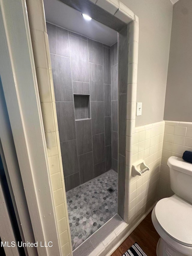 bathroom featuring toilet, hardwood / wood-style flooring, a tile shower, and tile walls