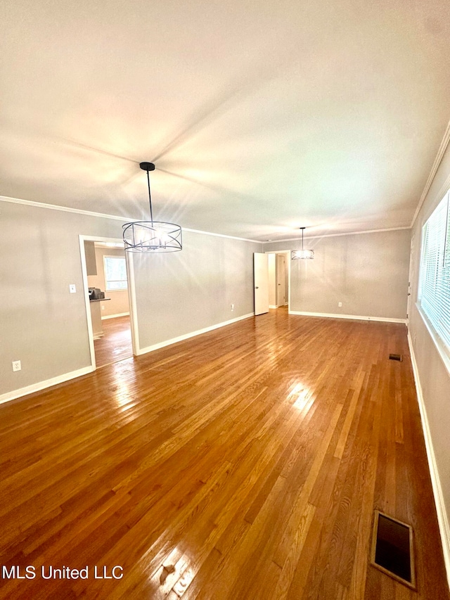 unfurnished living room featuring ornamental molding, hardwood / wood-style floors, and a notable chandelier