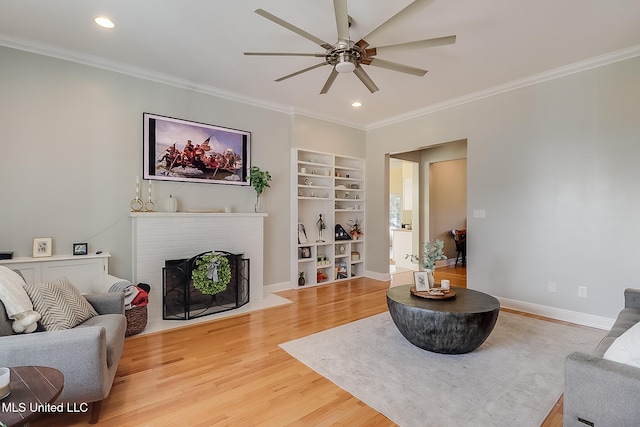 living room with a brick fireplace, wood-type flooring, ceiling fan, and crown molding