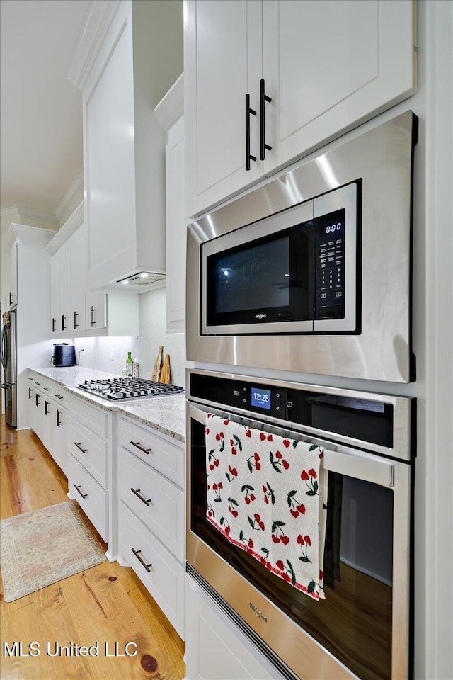 1622 Old Lake Rd, Brandon, MS 39042 - kitchen with appliances with stainless steel finishes, wall chimney exhaust hood, white cabinets, light wood-style flooring, and light stone countertops