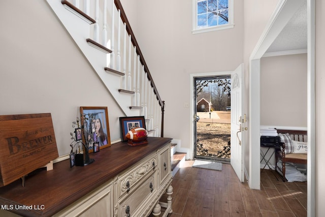 entryway with stairs, a high ceiling, dark wood finished floors, and ornamental molding