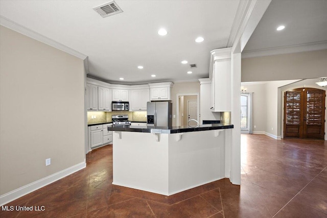 kitchen with kitchen peninsula, white cabinets, appliances with stainless steel finishes, dark tile patterned flooring, and crown molding