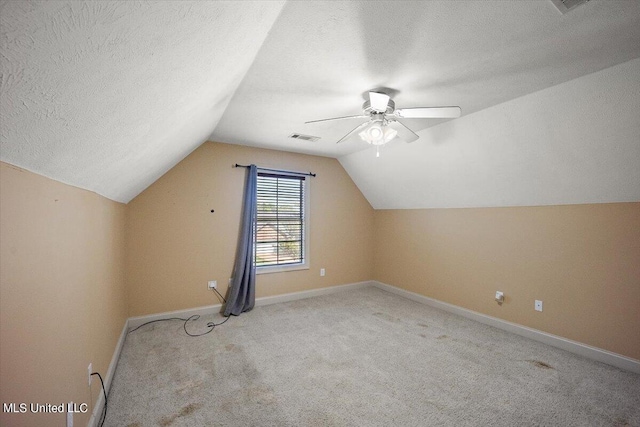 additional living space with vaulted ceiling, light carpet, a textured ceiling, and ceiling fan