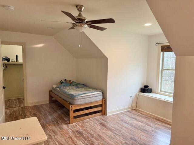 bedroom featuring lofted ceiling, a walk in closet, baseboards, and wood finished floors