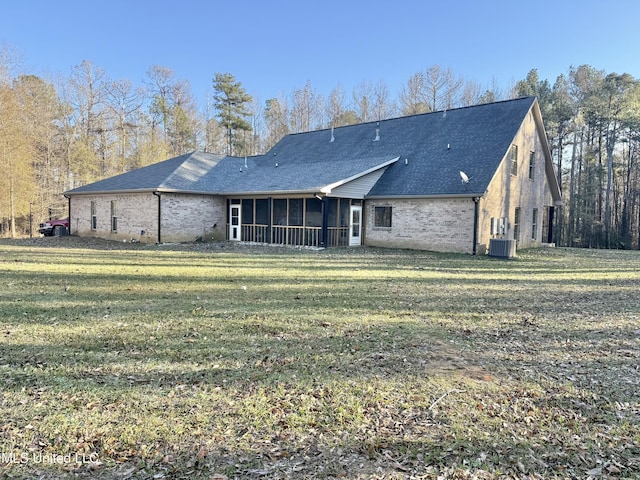 back of property with central AC, brick siding, a sunroom, a lawn, and roof with shingles