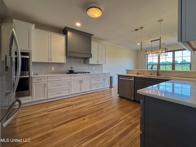 kitchen with appliances with stainless steel finishes, a sink, backsplash, light wood-type flooring, and light countertops