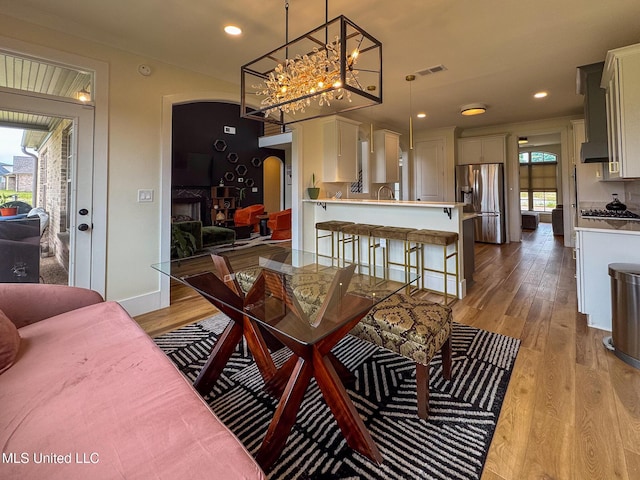 dining room with light wood-style flooring, arched walkways, a chandelier, recessed lighting, and baseboards